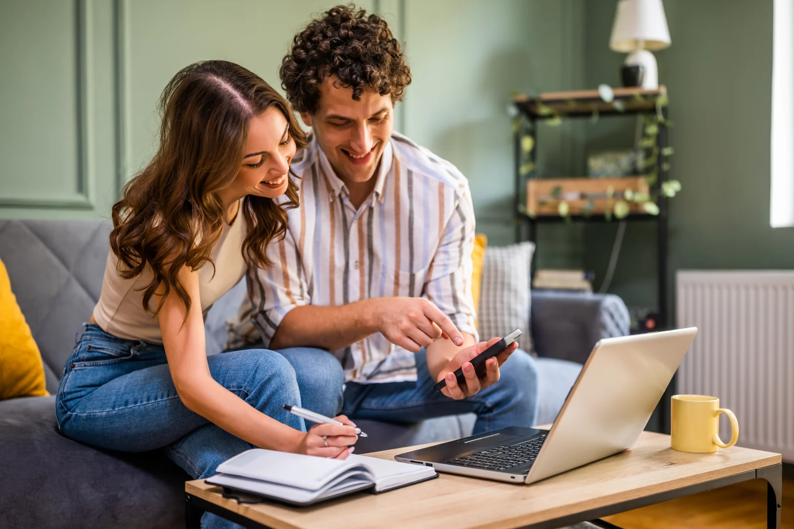 Couple reviewing information on a phone and laptop at home.