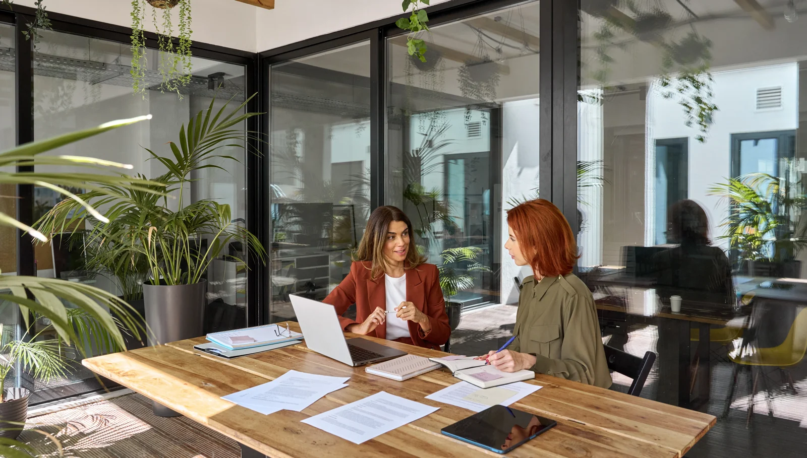 Two colleagues discussing documents at a table in an office.