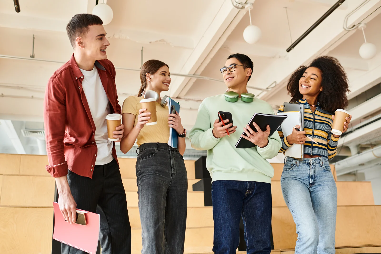 Four young adults talking while holding notebooks and drinks.