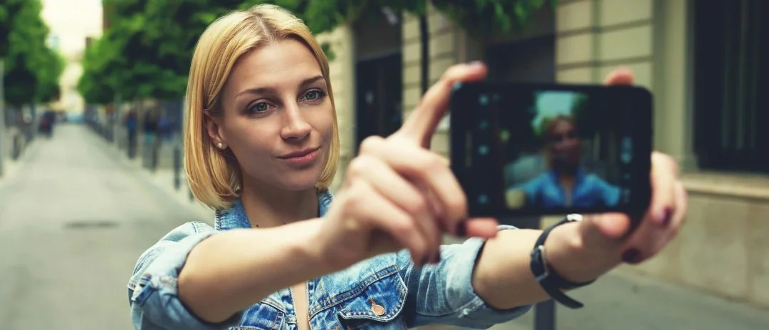 Stylish female hipster taking a picture of herself on smart phon