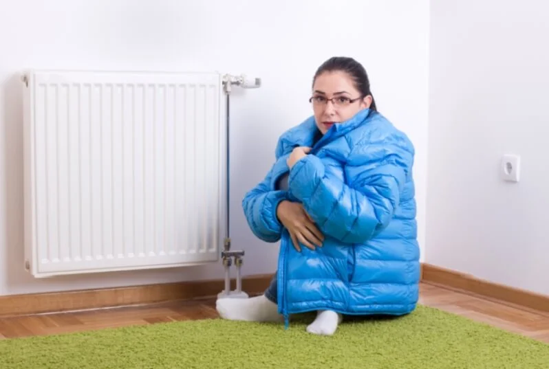 Young woman in blue winter jacket sitting next to cold radiator