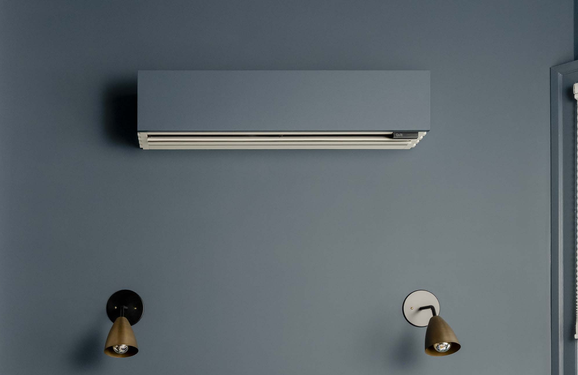 Gray wall with a rectangular air conditioner unit mounted near the top center and two brass and black wall lamps below it on each side.
