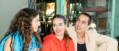 Three young adults sitting together indoors, engaged in conversation and smiling.