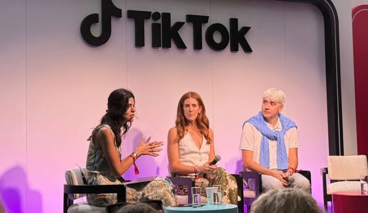 Three people seated on stage at a TikTok event, with two women and one man engaged in discussion, purple lighting in the background.
