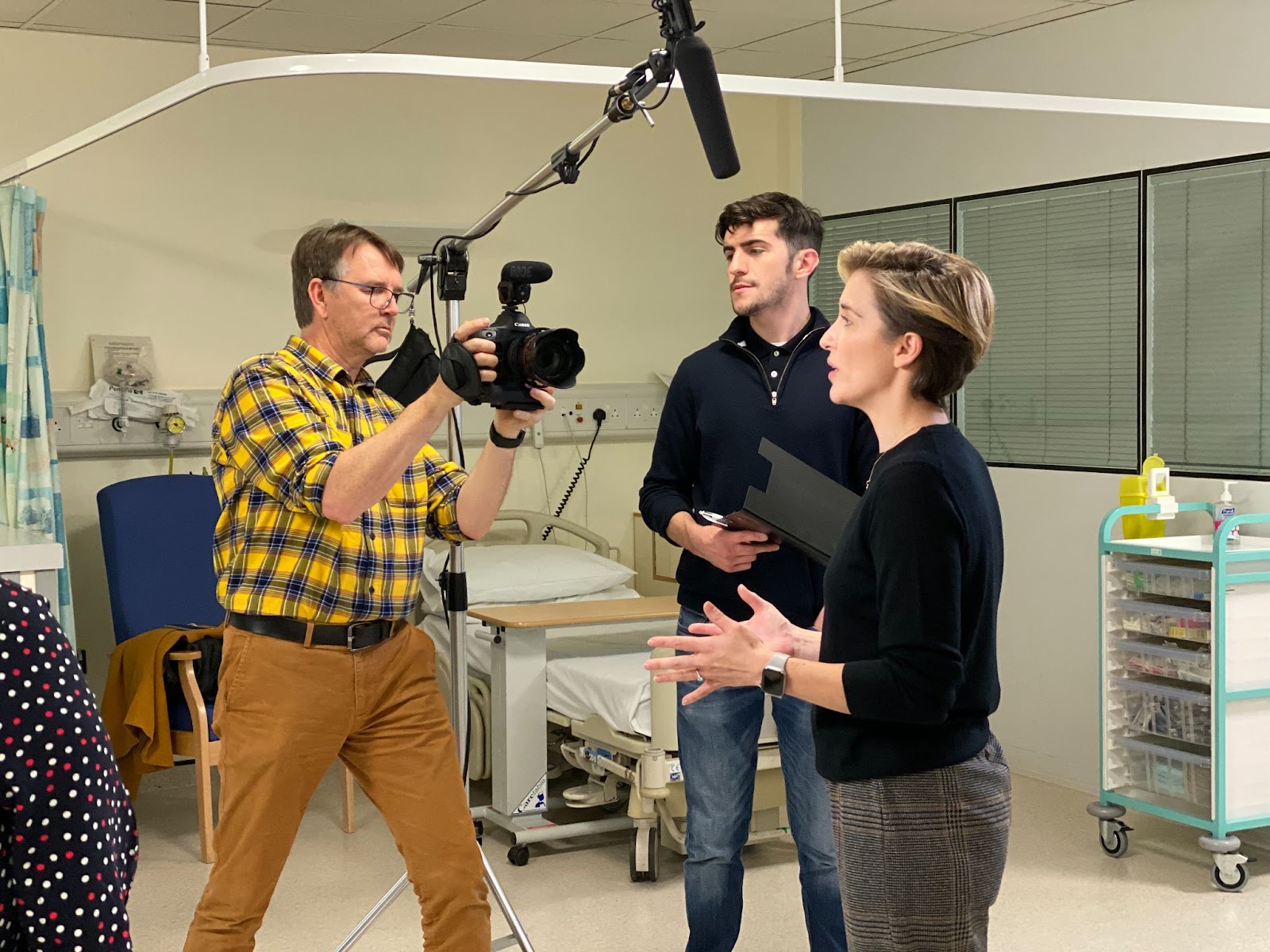 A video production team setting up a camera and discussing the shoot plan in a clinical location