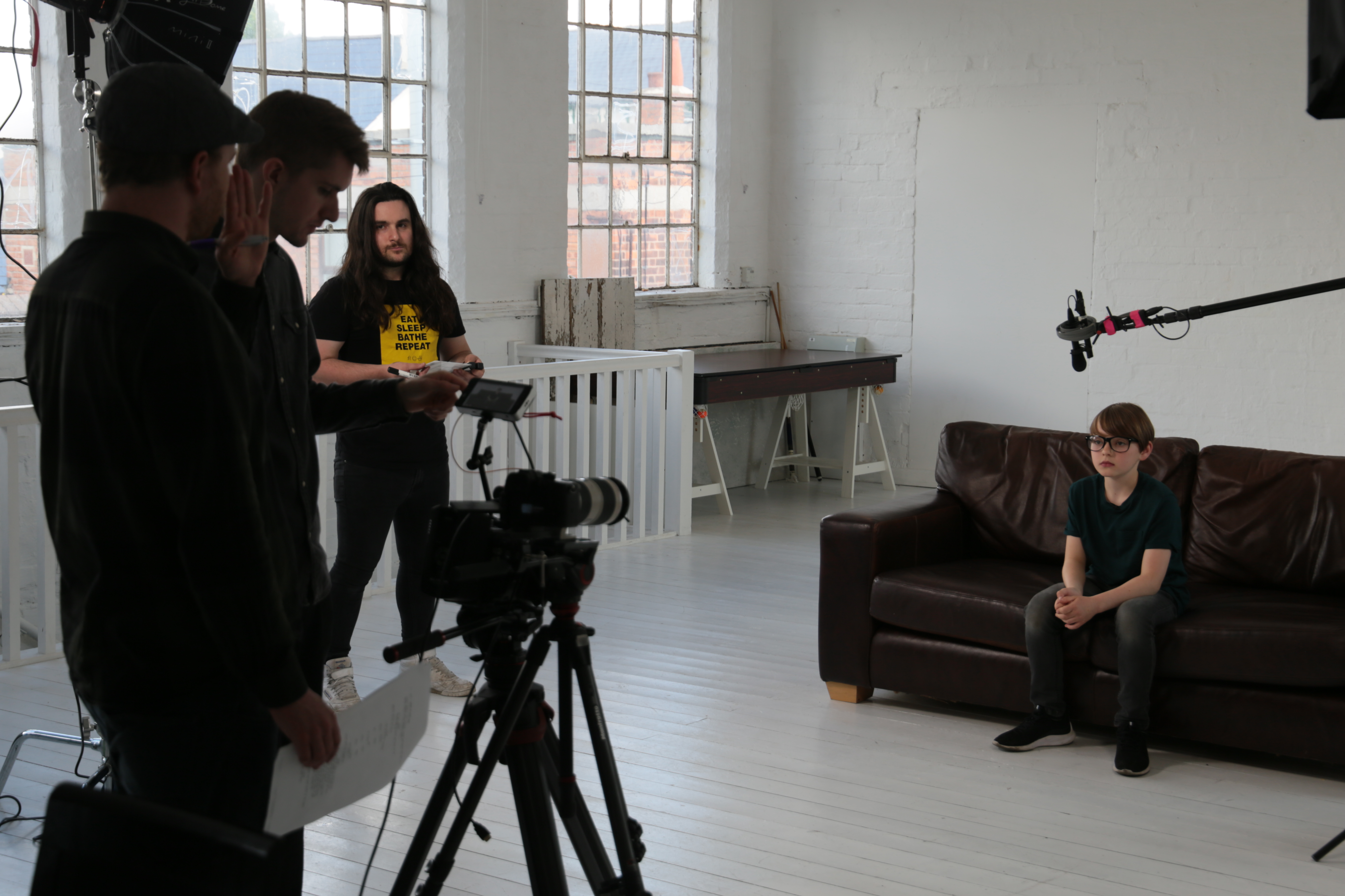 Film crew recording a boy sitting on a sofa.