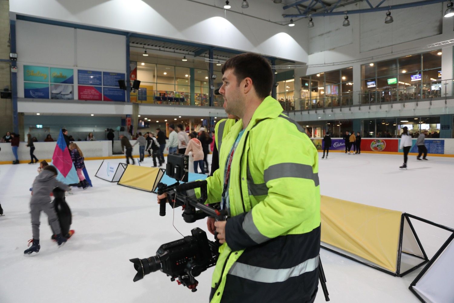 Man in a high-visibility jacket filming on an ice rink with a professional camera.