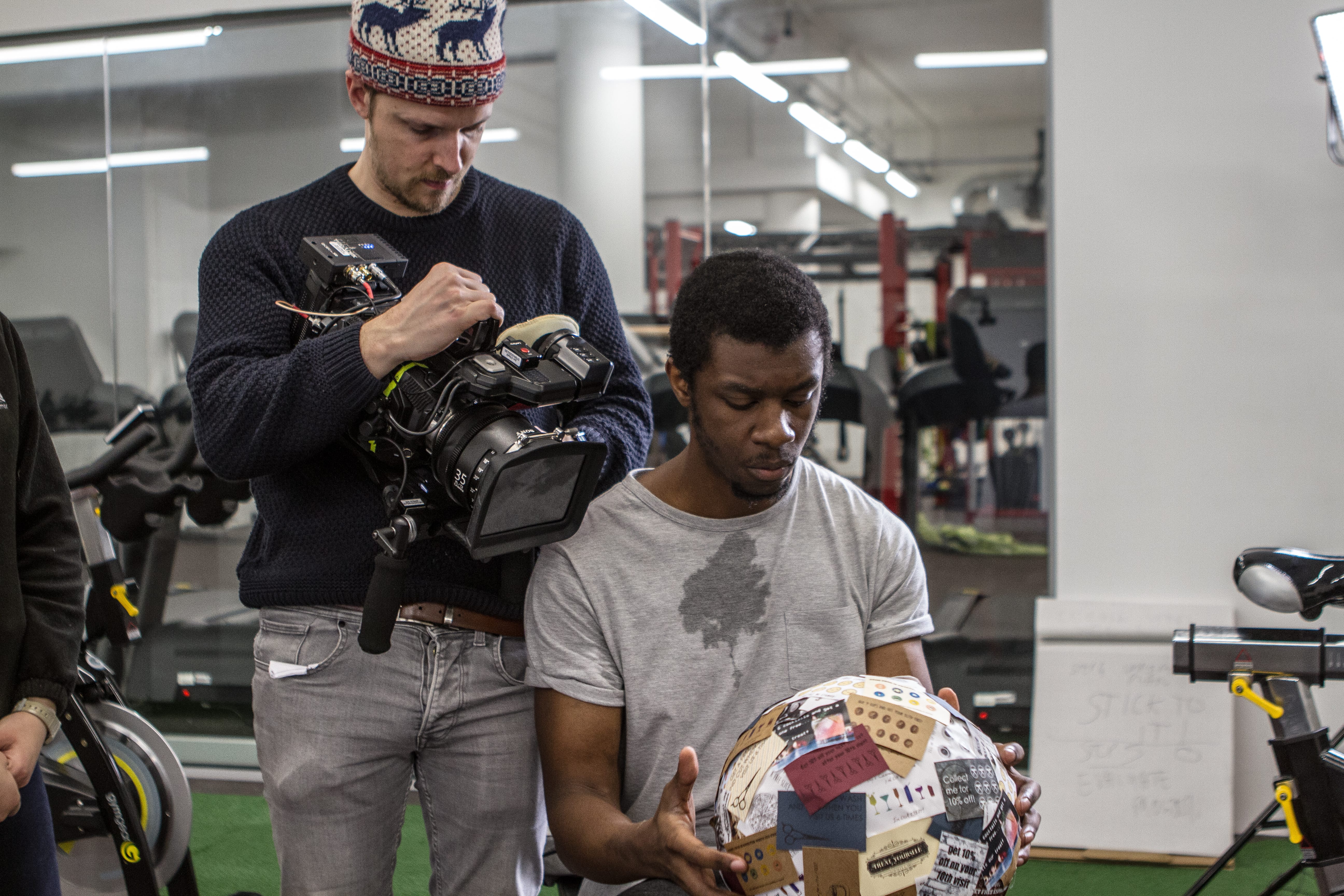 Videographer filming a man holding a football in a gym setting