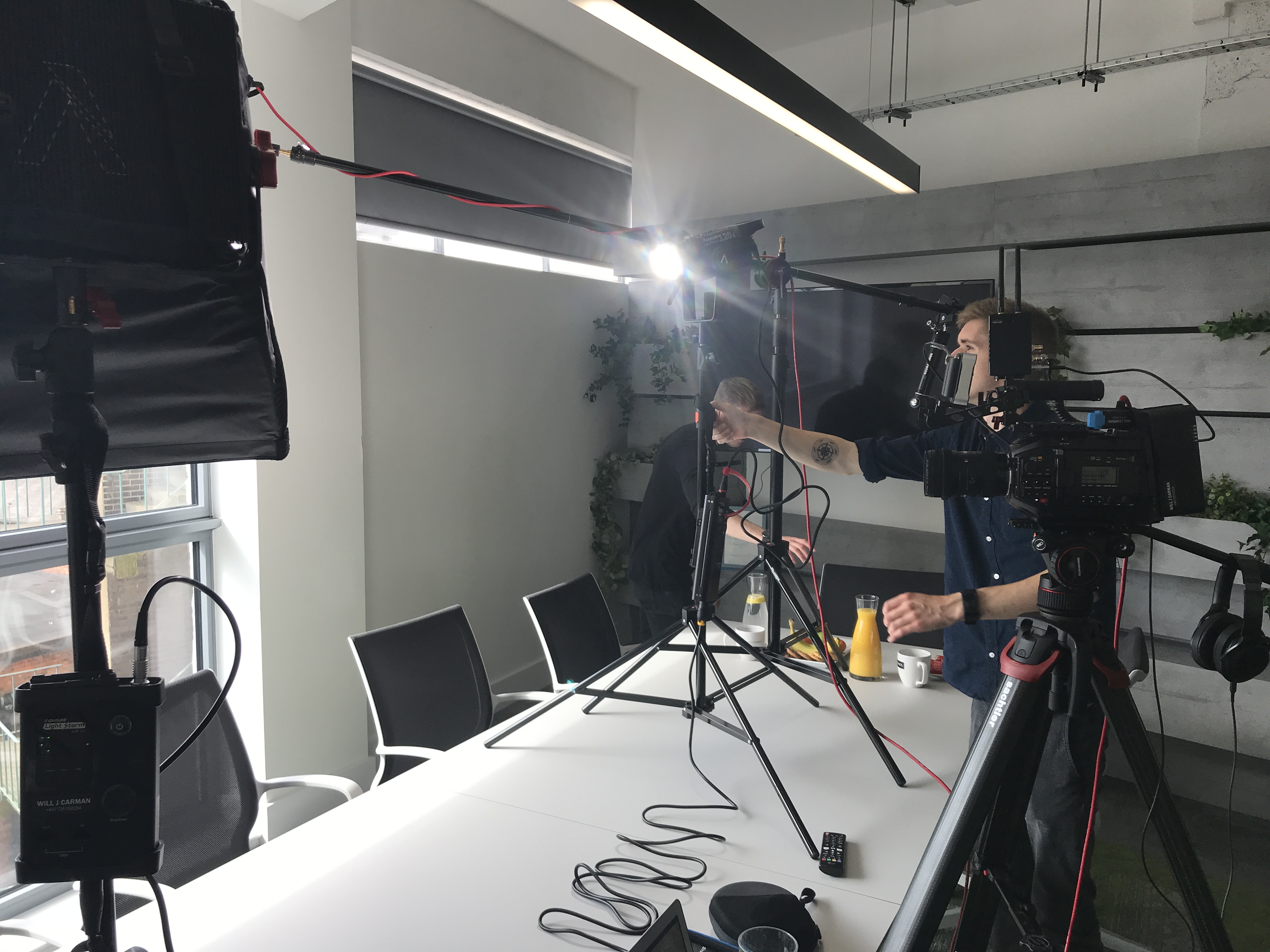 Behind-the-scenes shot of a video crew setting up lights and cameras in a meeting room.