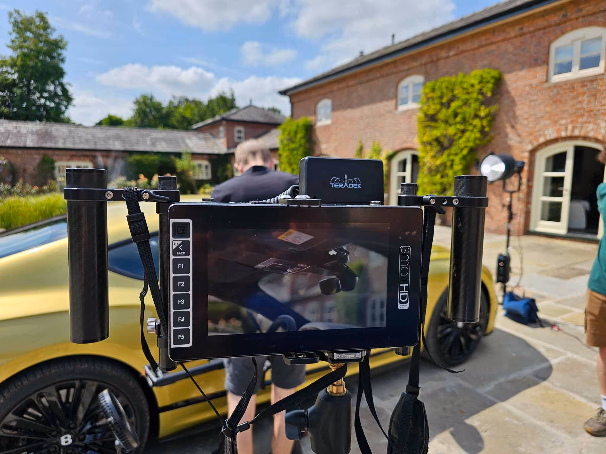 Camera monitor rig filming a yellow sports car on location outside a brick building