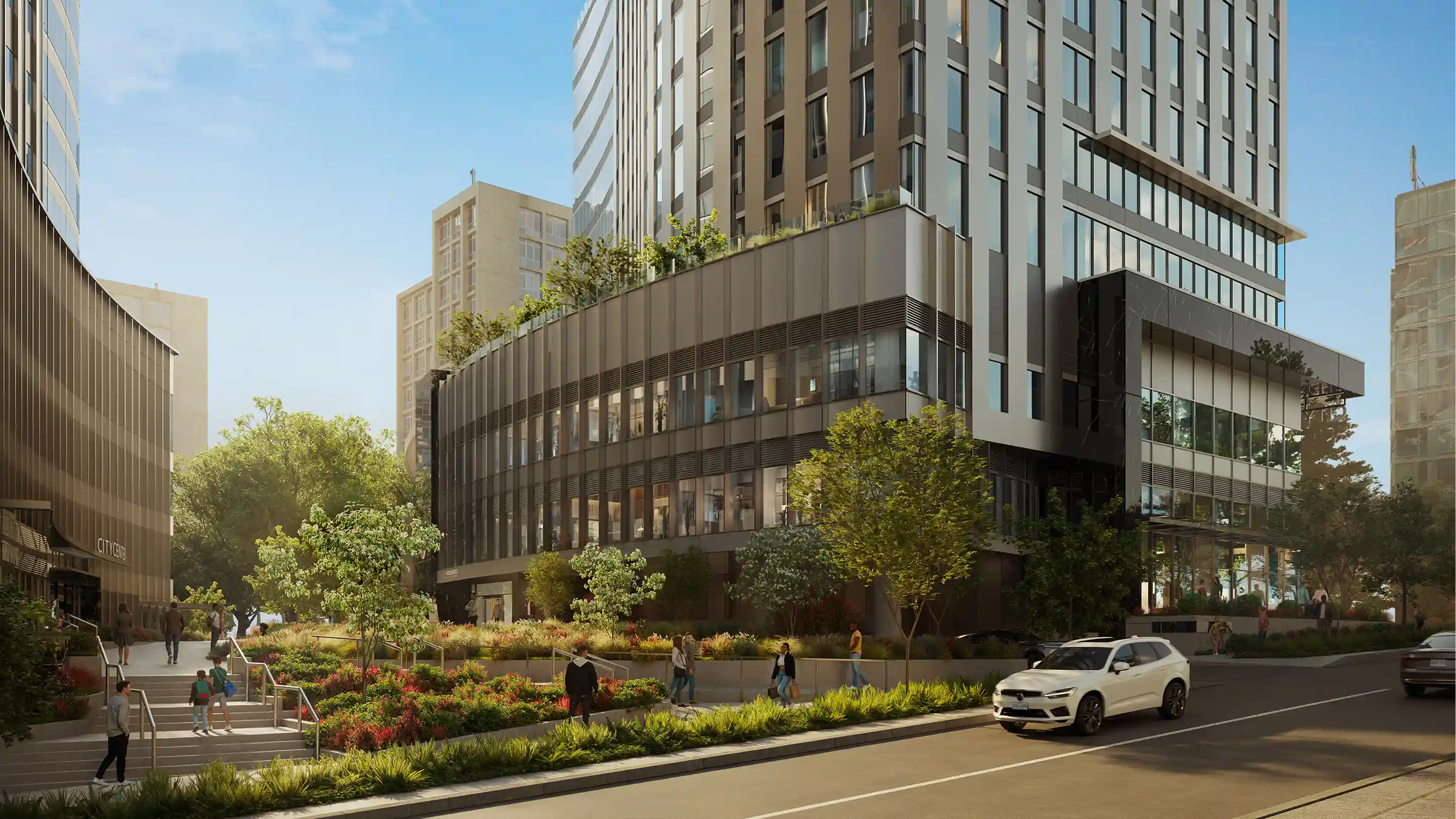 Modern multi-story buildings with glass windows and greenery along a pedestrian walkway and street with a white SUV.