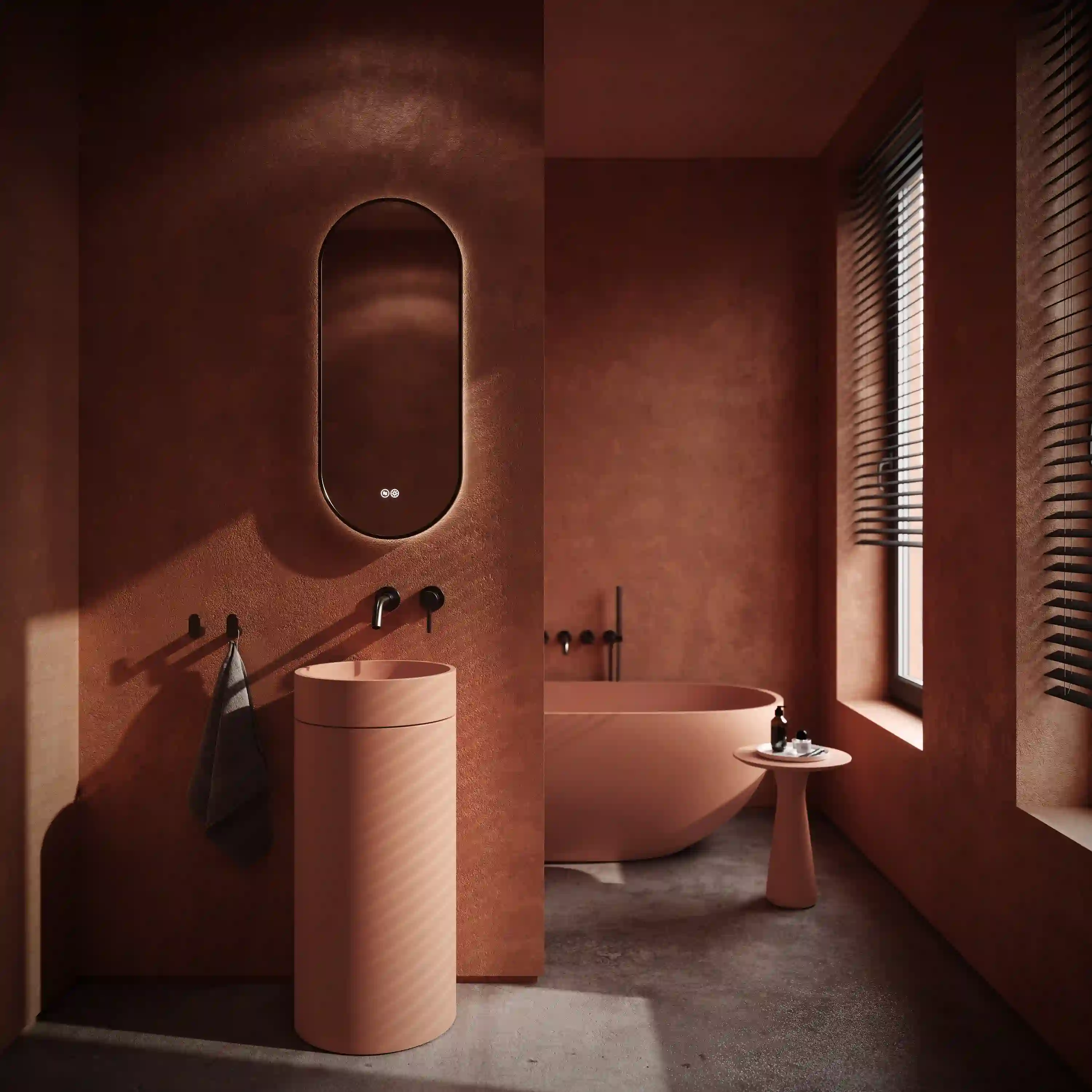 Modern bathroom with terracotta walls featuring a cylindrical sink, oval backlit mirror, freestanding bathtub, and small pedestal table near a window with blinds.