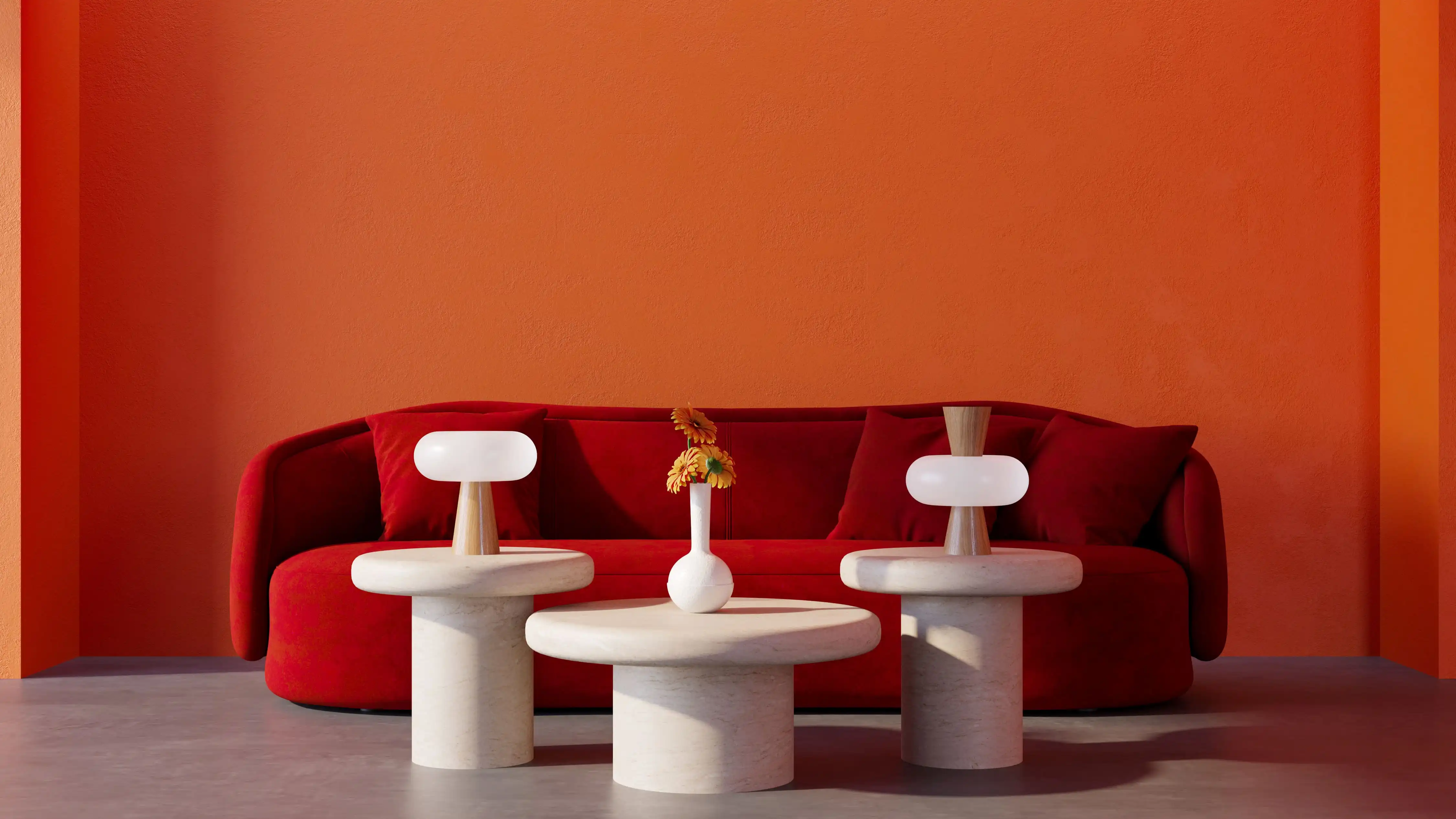 Modern living room with a red sofa against an orange wall, featuring three round white stone tables, two with minimalist lamps and one with a small white vase holding orange flowers.