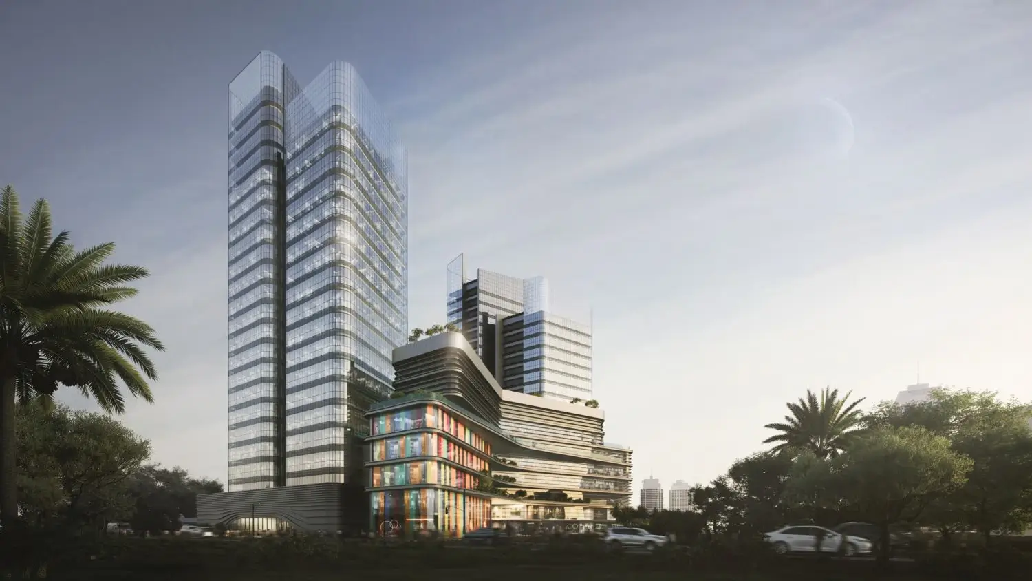 Modern commercial building with tall glass towers and colorful lower floors beside palm trees under a cloudy sky.