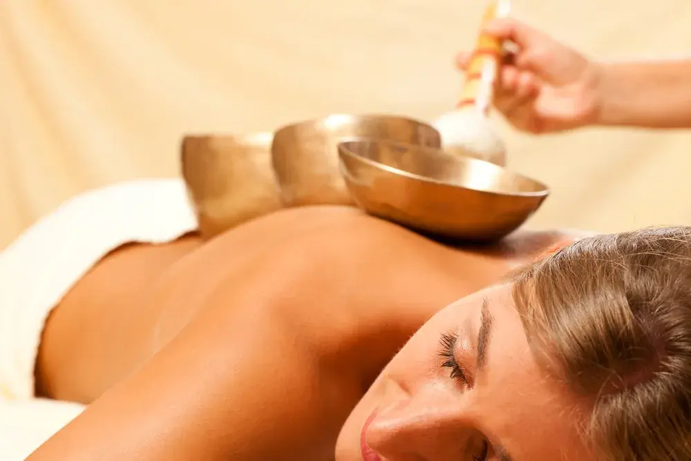 Frau liegt entspannt auf Massageliege mit Klangschalen auf dem Rücken – wohltuende Atmosphäre bei einer Klangschalenmassage