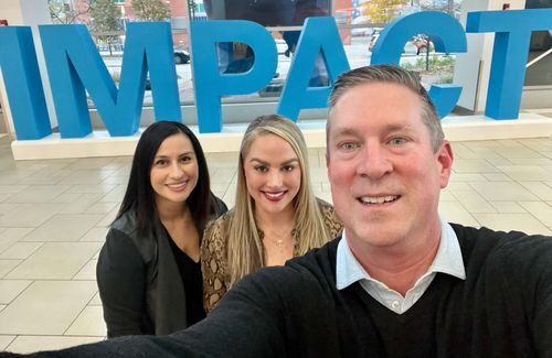 Three people taking a selfie in front of impact sign.