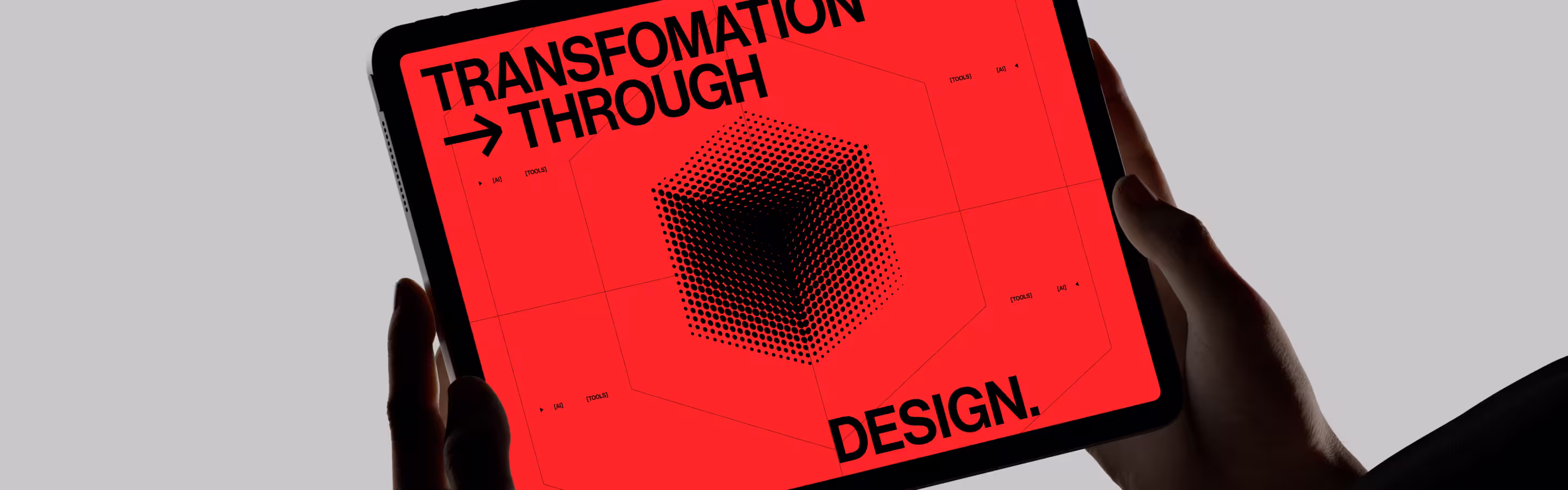 Hands holding a tablet displaying a bold red screen with the text “TRANSFORMATION THROUGH DESIGN.” in large black capital letters. The center features a geometric black dot pattern forming a 3D-like cube.
