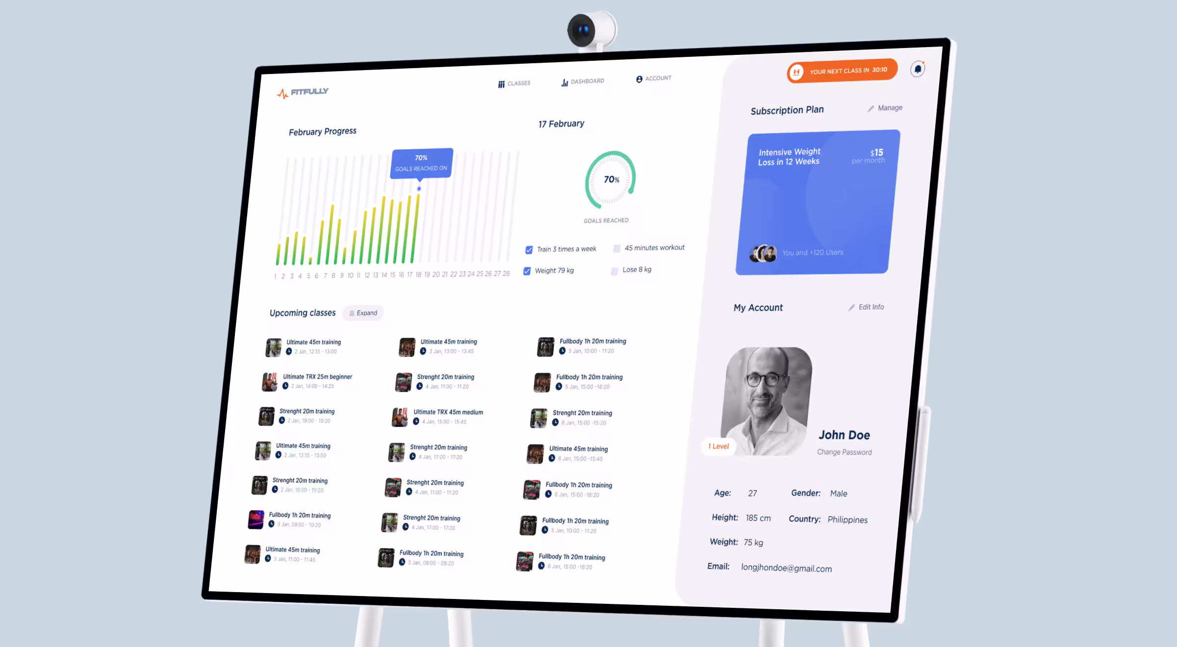 A fitness app dashboard displayed on a smart screen showing February workout progress, upcoming training classes, a subscription plan, and personal account details for a user named John Doe. The interface is clean and modern, with progress charts, schedules, and profile information.