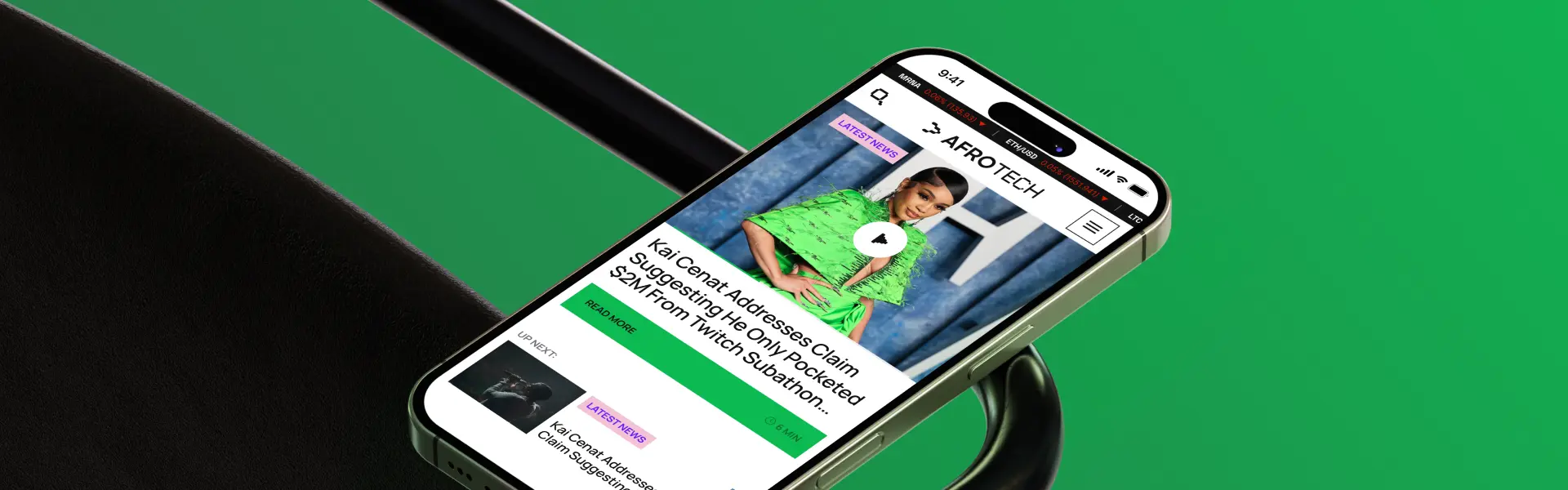 Close-up of a smartphone displaying the AFROTECH website on a green background. The screen shows a featured news article titled “Kai Cenat Addresses Claim Suggesting He Only Pocketed $2M From Twitch Subathon,” accompanied by a large image of a woman in a bright green outfit. The website features elements like a “Latest News” label, a “Read More” button, and a cryptocurrency ticker at the top showing price changes for MRNA, ETH, and LTC. The interface includes a navigation menu and a preview of the next article in the feed.