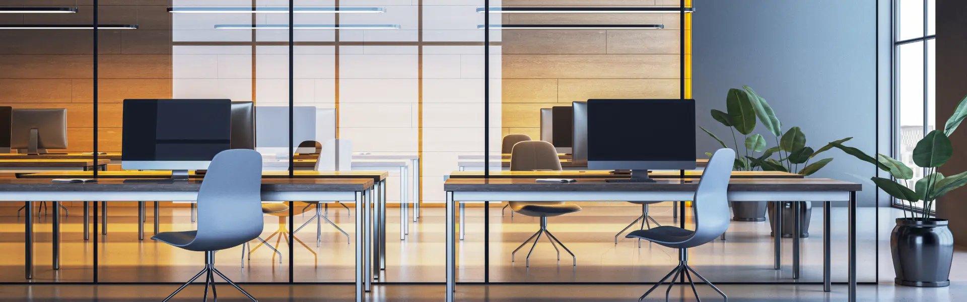 Modern open-plan office with sleek black and white computer monitors on minimalist desks, ergonomic chairs, and glass walls dividing workspaces. Warm ambient lighting and a potted plant enhance the clean, contemporary design.