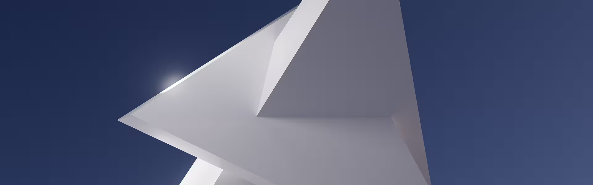 Abstract architectural structure with sharp geometric angles and smooth white surfaces, photographed from a low perspective against a clear deep blue sky with sunlight reflecting off the edges.