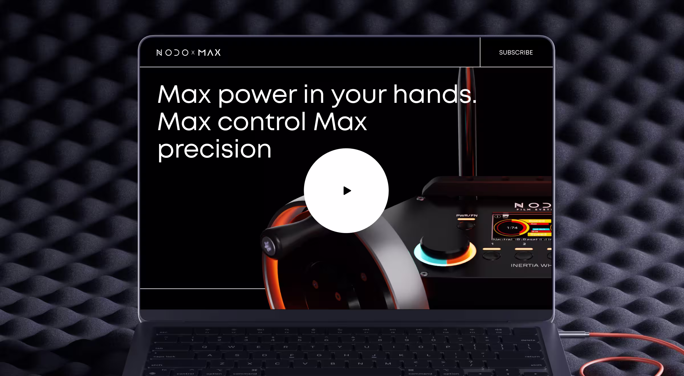 Laptop screen showing a promotional video for NODO MAX, with the text 'Max power in your hands. Max control Max precision' alongside a futuristic control device with illuminated dials and buttons, set against a dark acoustic foam background.