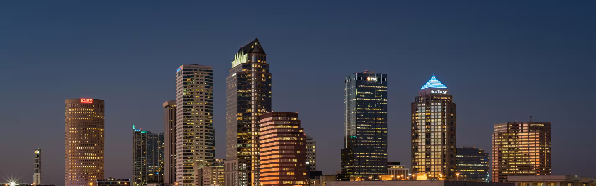 Downtown Tampa skyline at dusk featuring illuminated high-rise office buildings and waterfront architecture