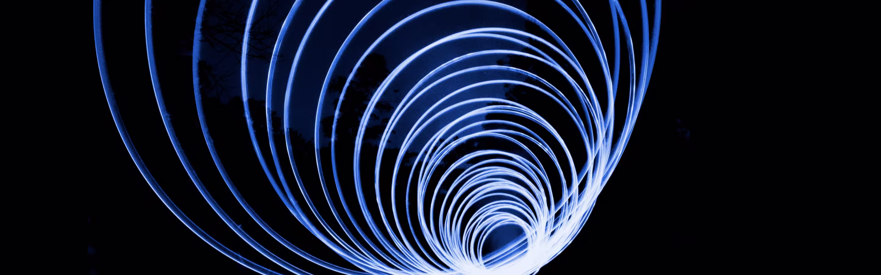 A vibrant blue spiral of light trails against a dark background, creating a mesmerizing vortex effect.
