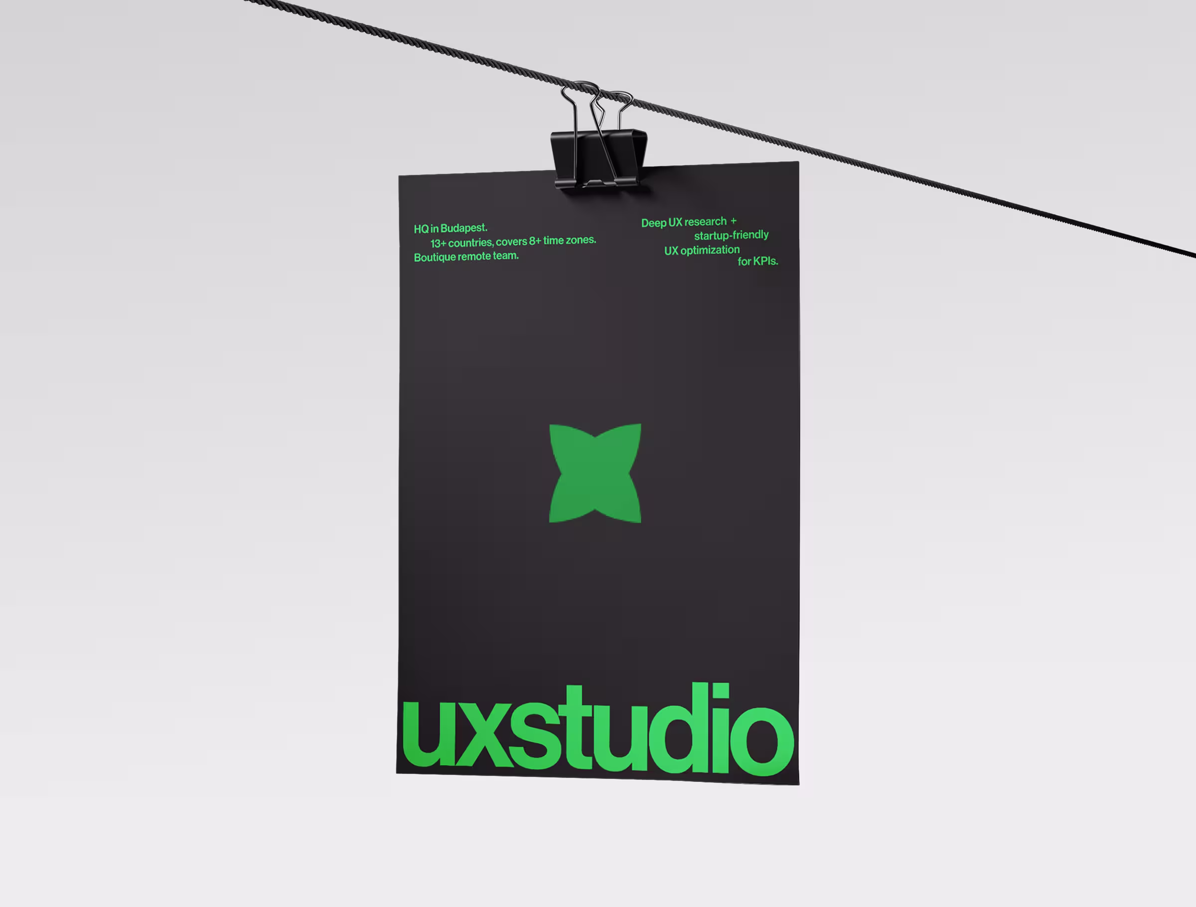 Black poster with a green butterfly-shaped logo and bold ‘uxstudio’ branding, hanging from a clipped wire against a clean light background