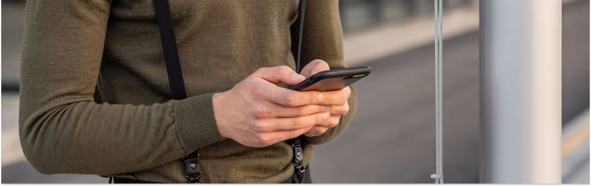 Close-up of a person in a green sweater holding and typing on a smartphone outdoors
