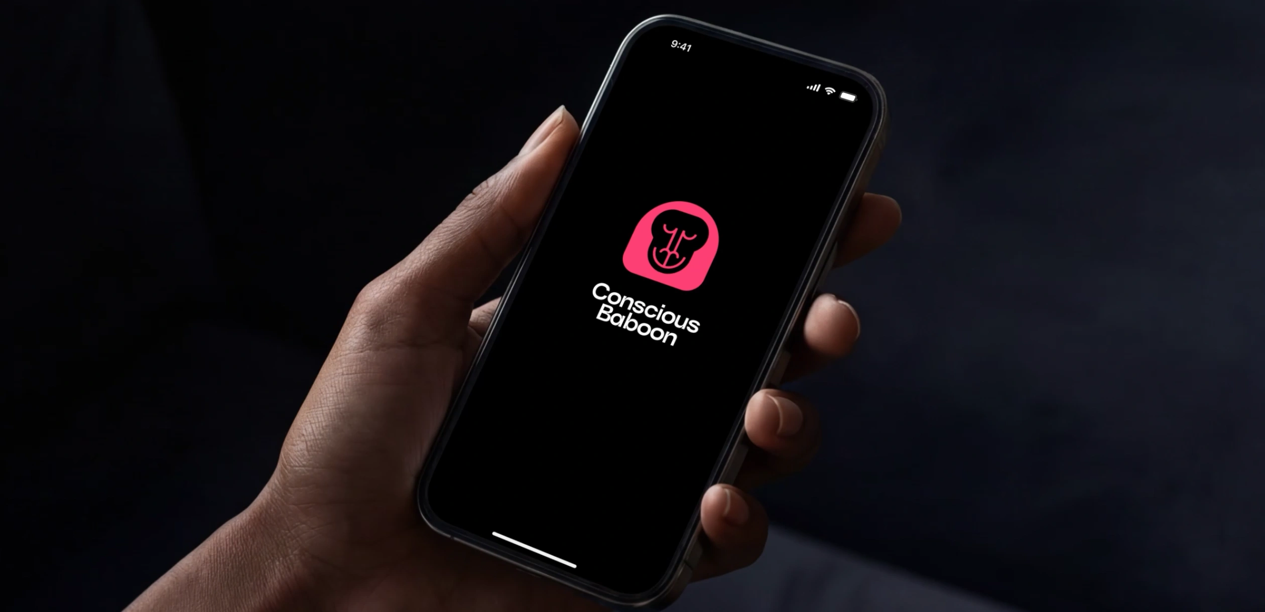 Hand holding a smartphone with the Conscious Baboon logo displayed on a black app loading screen.