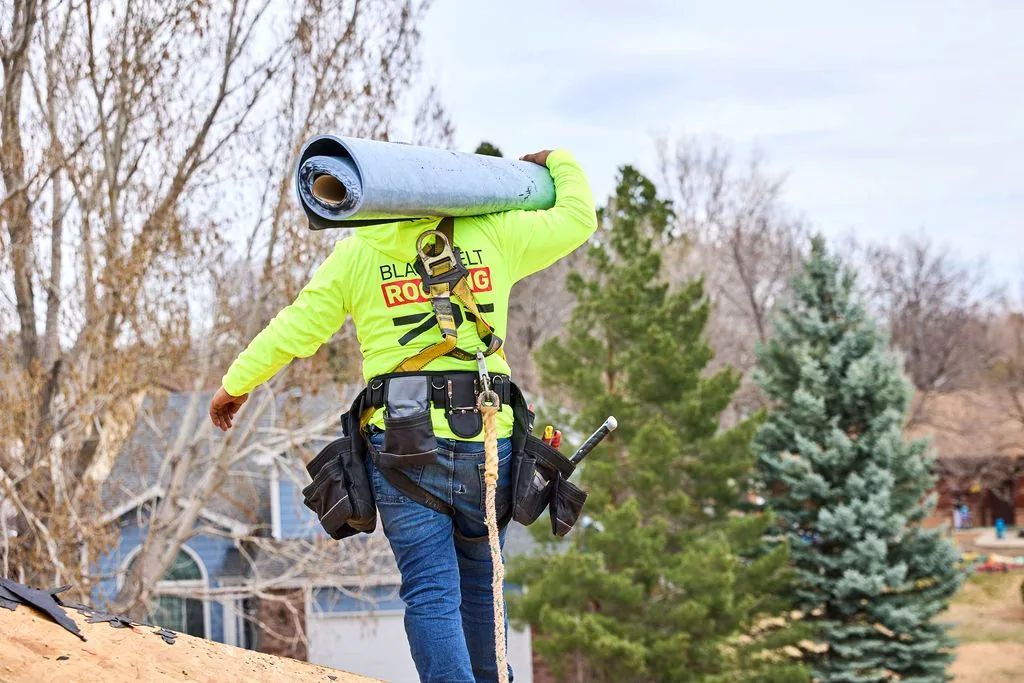 Black Belt Roofing crew member carrying a roll of roofing material during installation.