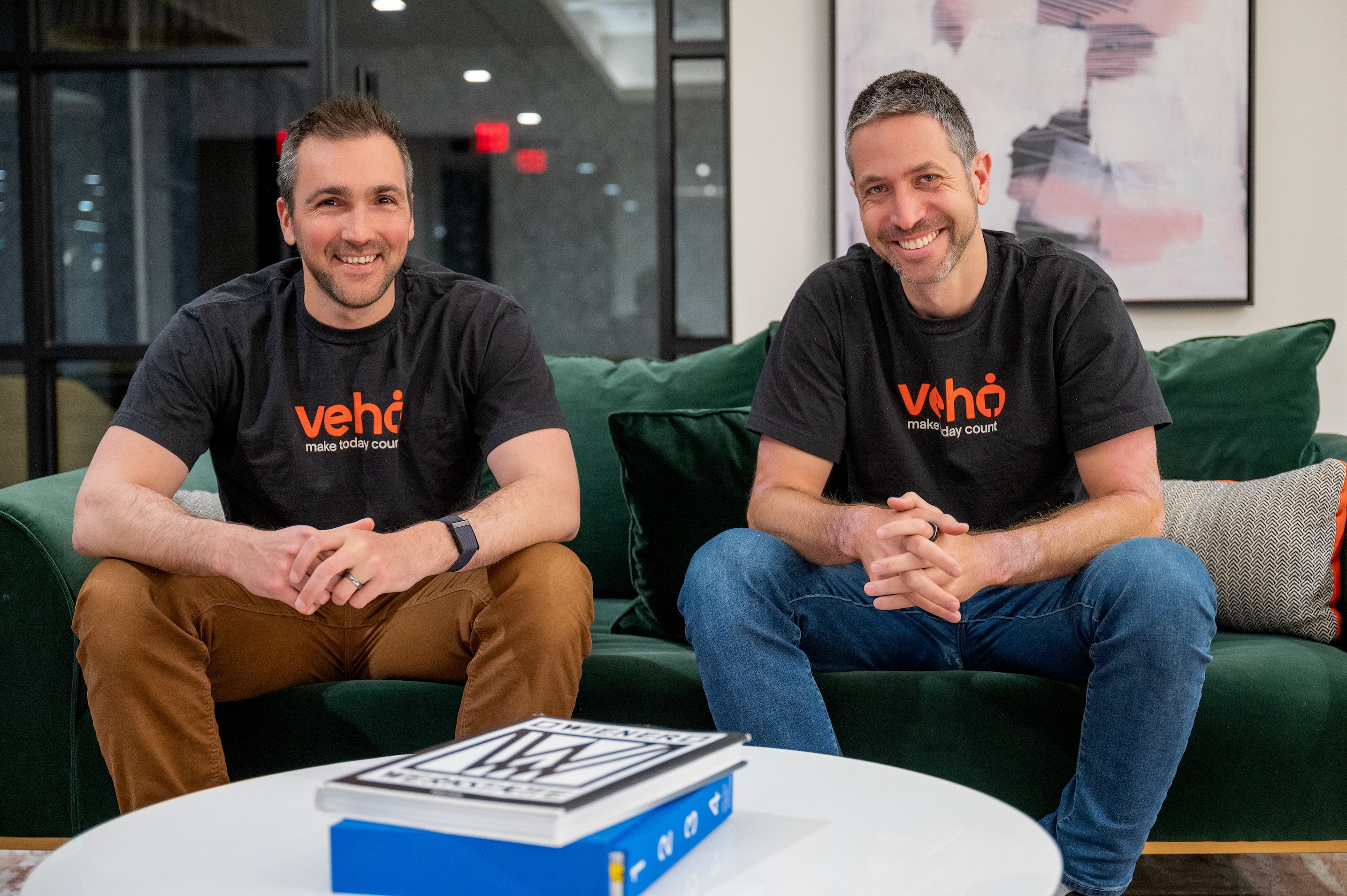 A man wearing t-shirt with Veho logo standing near a table.