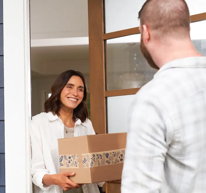Woman smiling and receiving a cardboard package from a man at her doorway.