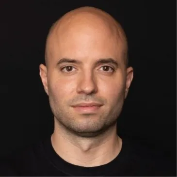 Portrait of a bald man with light skin and brown eyes wearing a black shirt against a black background.