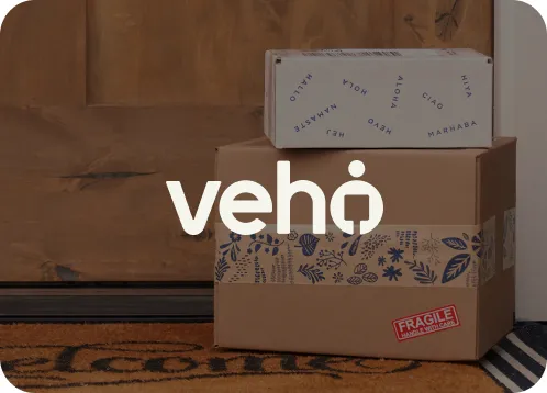 Three stacked cardboard boxes on a doormat in front of a wooden door, with a fragile sticker on the bottom box.