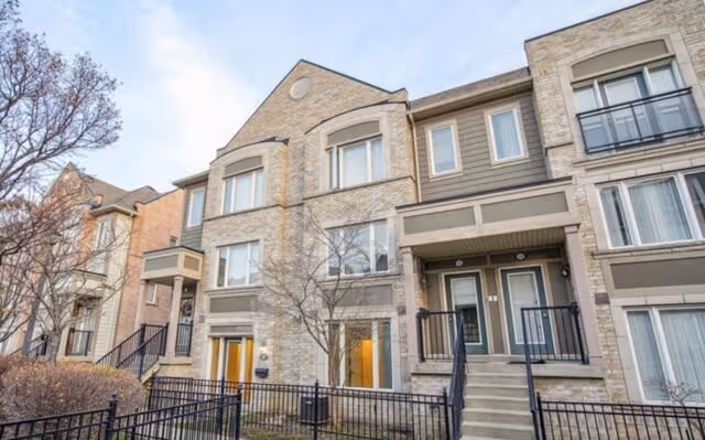 Exterior view of a modern multi-story townhouse with stone and brick facade, windows, and small balconies.