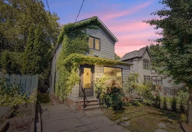 Two-story house covered with green ivy beside a tree-lined yard under a pink and blue sunset sky.