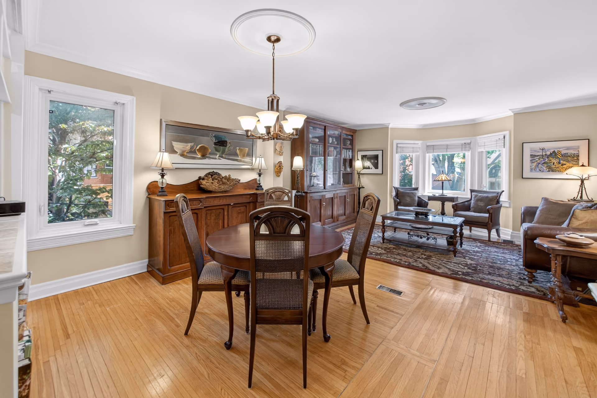 Modern dining room with wooden table set for six, gray chairs, indoor plants, and an open kitchen with bar stools.