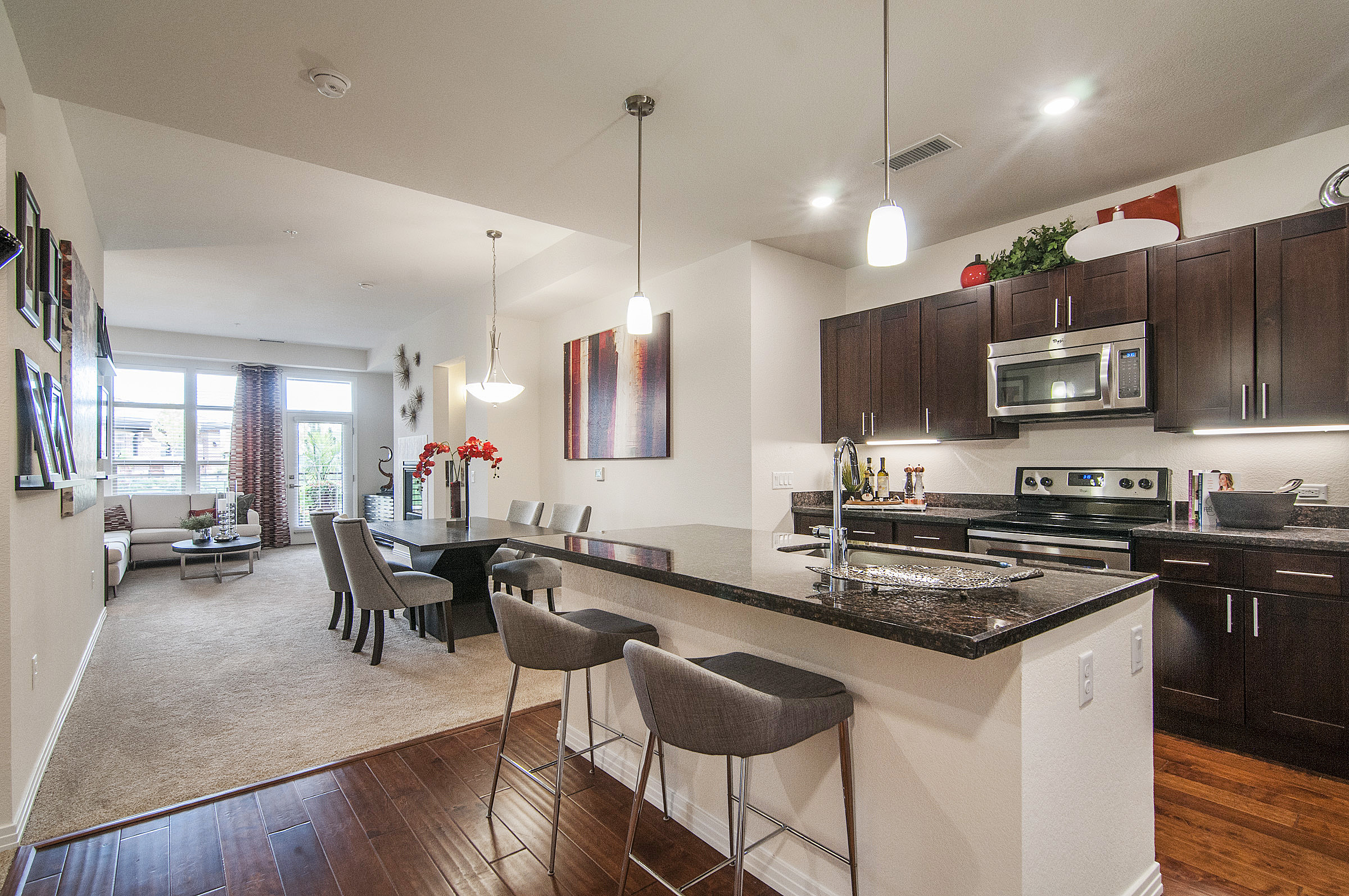 Kitchen featuring island with chairs, black appliances, and brown cabinets with view into dining area with table and chairs and living area with sofa and coffee table
