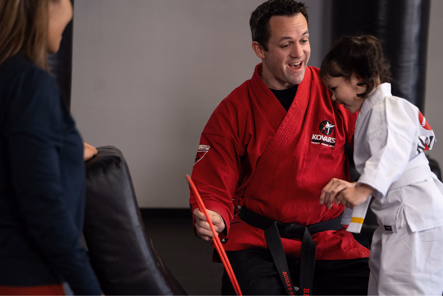 Kovar's instructor kneeling to teach a preschooler in a martial arts uniform
