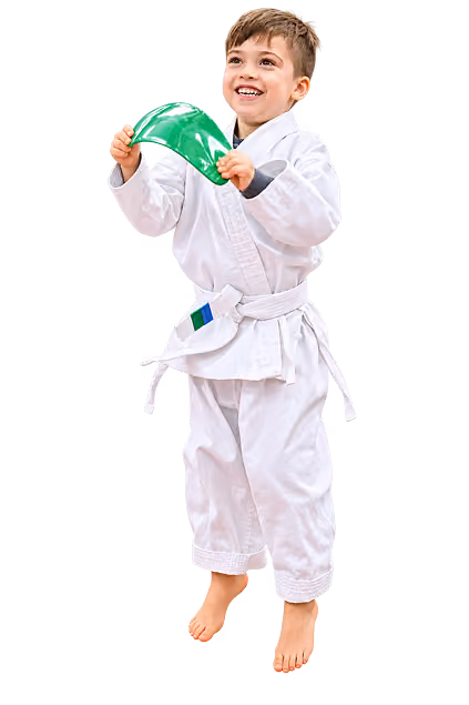 Smiling young boy in a white martial arts uniform with a white belt holding a green object, standing barefoot.