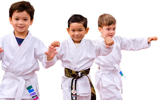 Three young boys in white martial arts uniforms practicing punches, with one boy wearing a black belt and the others wearing white belts.