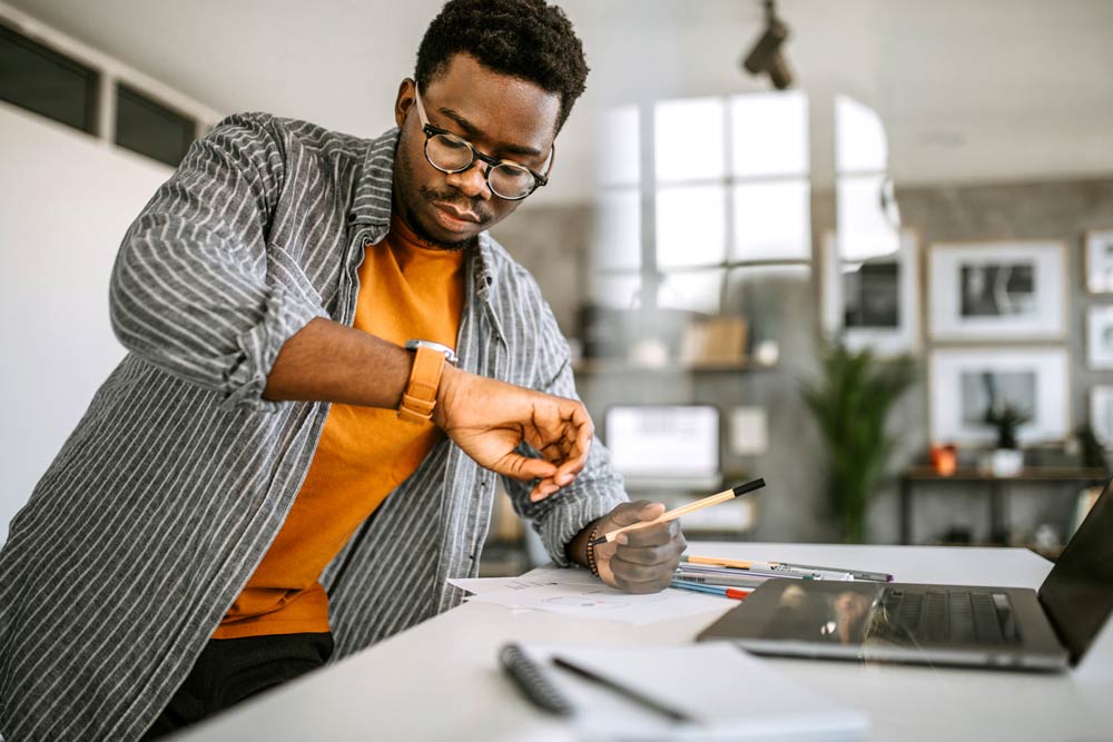Man checking his watch while working at a desk, symbolizing time blindness and deadline challenges with ADHD.