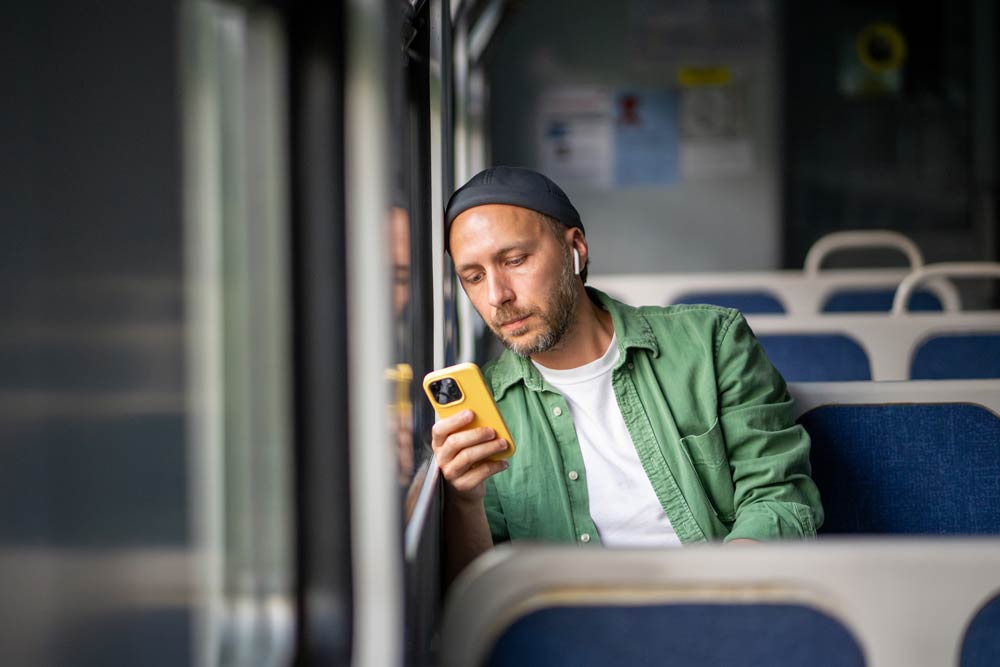A man wearing headphones looks at his phone while riding public transit, representing how people with ADHD experience noise sensitivity and struggle with distractions.