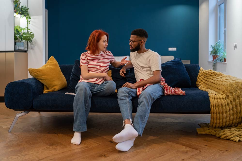 A couple sitting on a sofa having a serious conversation, symbolizing strategies for improving communication between a partner with ADHD and a neurotypical partner.