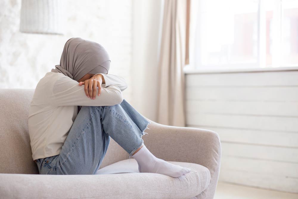 A woman sitting curled up on a couch with her head resting on her arms, representing sensory overload and overstimulation in ADHD.