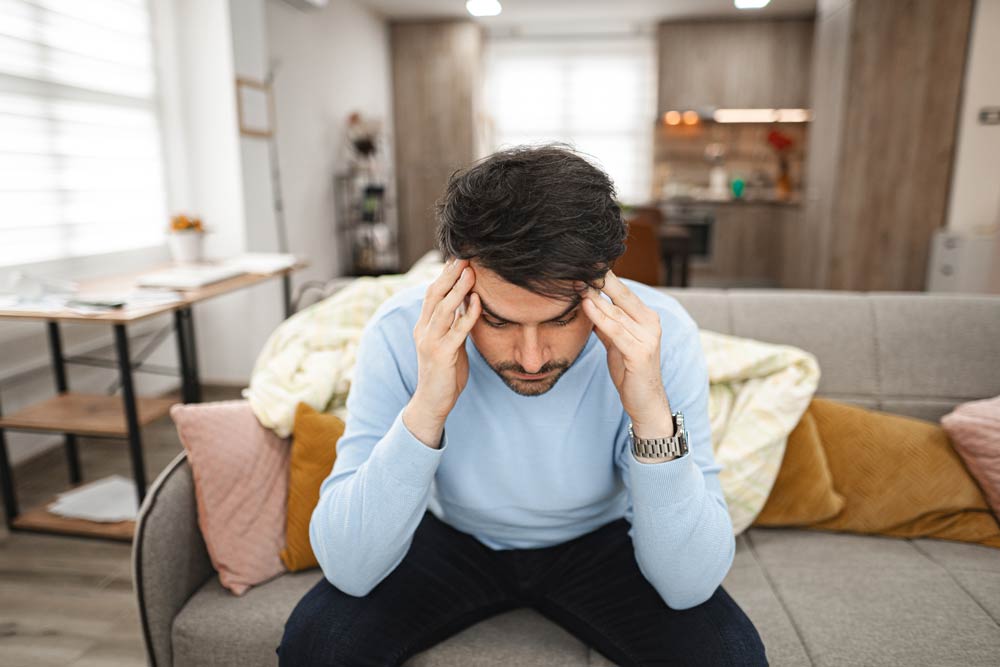 A man sitting on a couch holding his head in his hands, representing the link between ADHD and sensory processing difficulties.