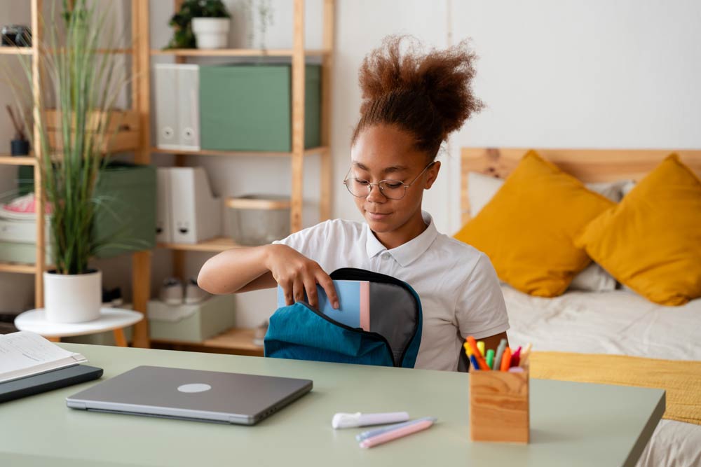 A teenage student packs her school backpack at a desk with books and supplies, illustrating organization strategies for teens with ADHD.