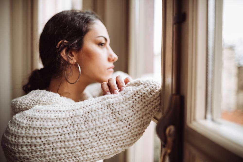 Woman looking out of a window thoughtfully, symbolizing the overlap between ADHD symptoms and other mental health conditions.